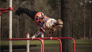 Young man wearing colorful outfit doing calisthenics on red bars in Vilnius park.